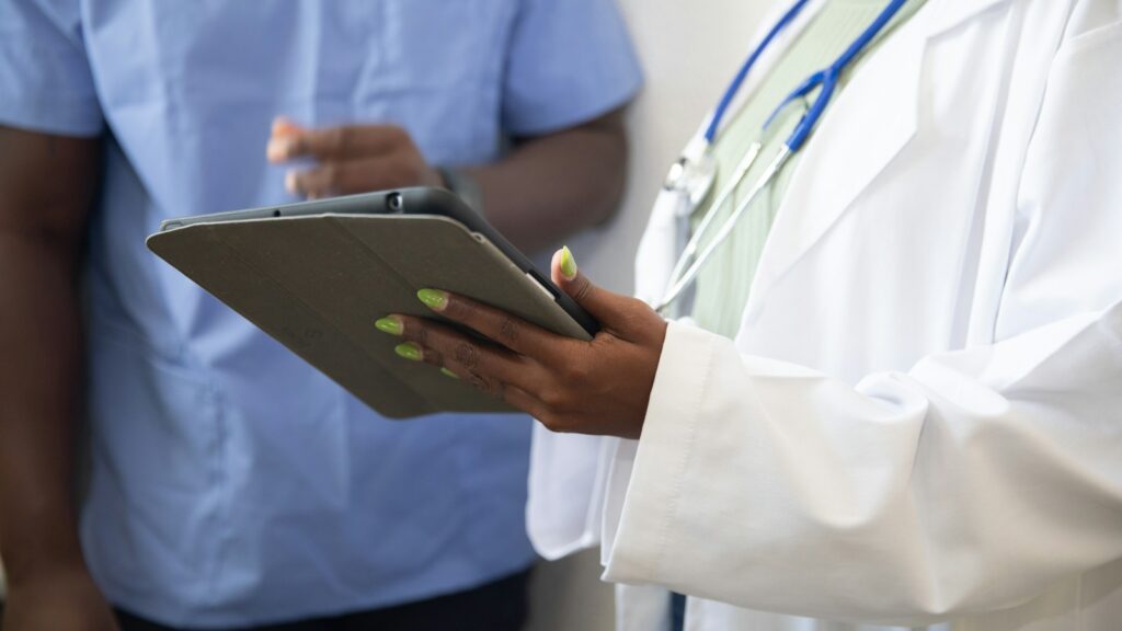 Black healthcare professionals reviewing information on a tablet in a clinical setting.