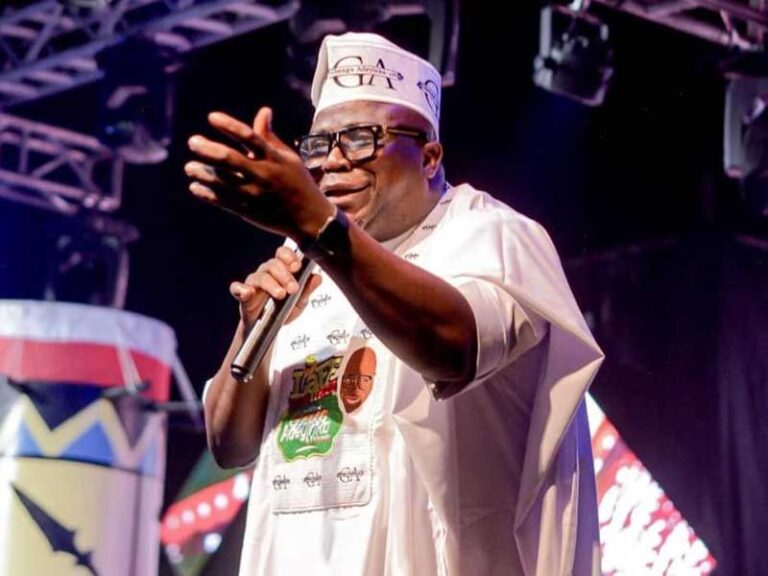 Gbenga Adeyinka performing on stage with a microphone during a Laffmattazz comedy show.