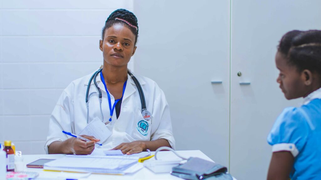 African healthcare worker seated across from a young patient in a clinic.
