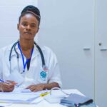 African healthcare worker seated across from a young patient in a clinic.