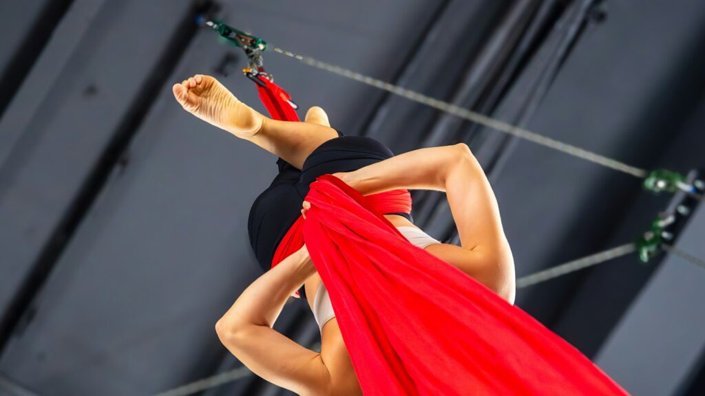 Aerial performer training with red silks under stage rigging