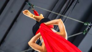 Aerial performer training with red silks under stage rigging