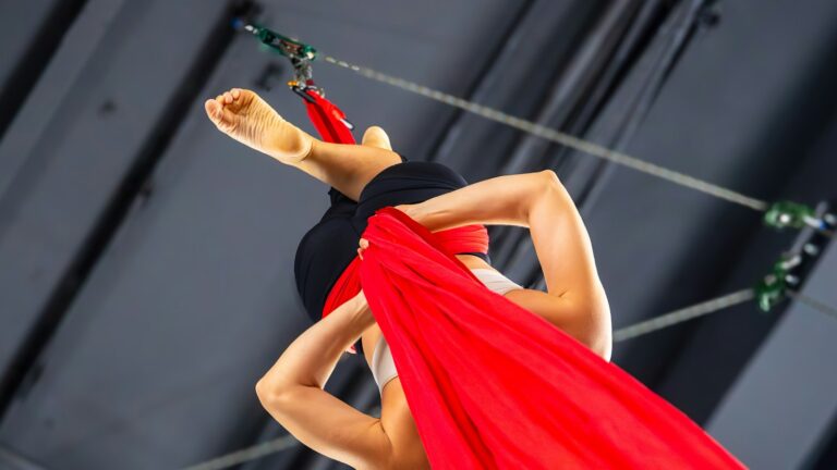 Aerial performer training with red silks under stage rigging