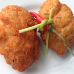 Two golden àkàrà bean cakes on a white plate with a red pepper and green garnish, photographed on 11 July 2013.