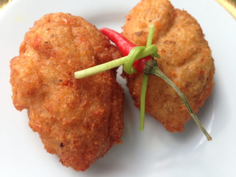 Two golden àkàrà bean cakes on a white plate with a red pepper and green garnish, photographed on 11 July 2013.