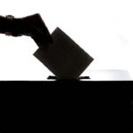 A voter places a ballot into a box, illustrating election observation