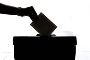 A voter places a ballot into a box, illustrating election observation
