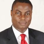 Pius Osunyikanmi wearing a dark suit, white shirt and red tie.