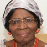 Professor Kamene Okonjo wearing glasses, a patterned headwrap and coral jewellery.