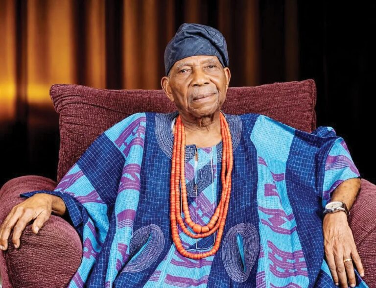 Reuben Fasoranti seated in traditional Yoruba attire and a blue cap